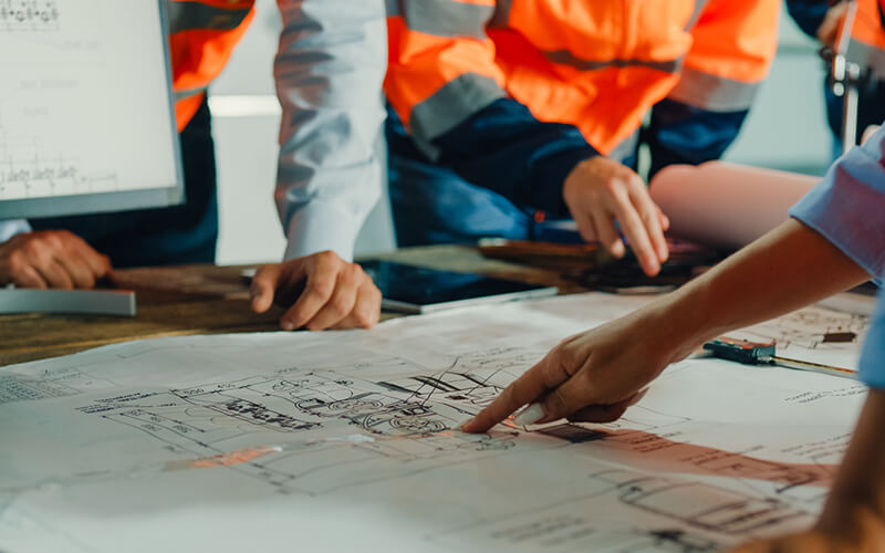 Closeup of team of industrial engineers meeting analyze machinery blueprints consult project on table in manufacturing factory. Working in manufacturing plant or production plant.