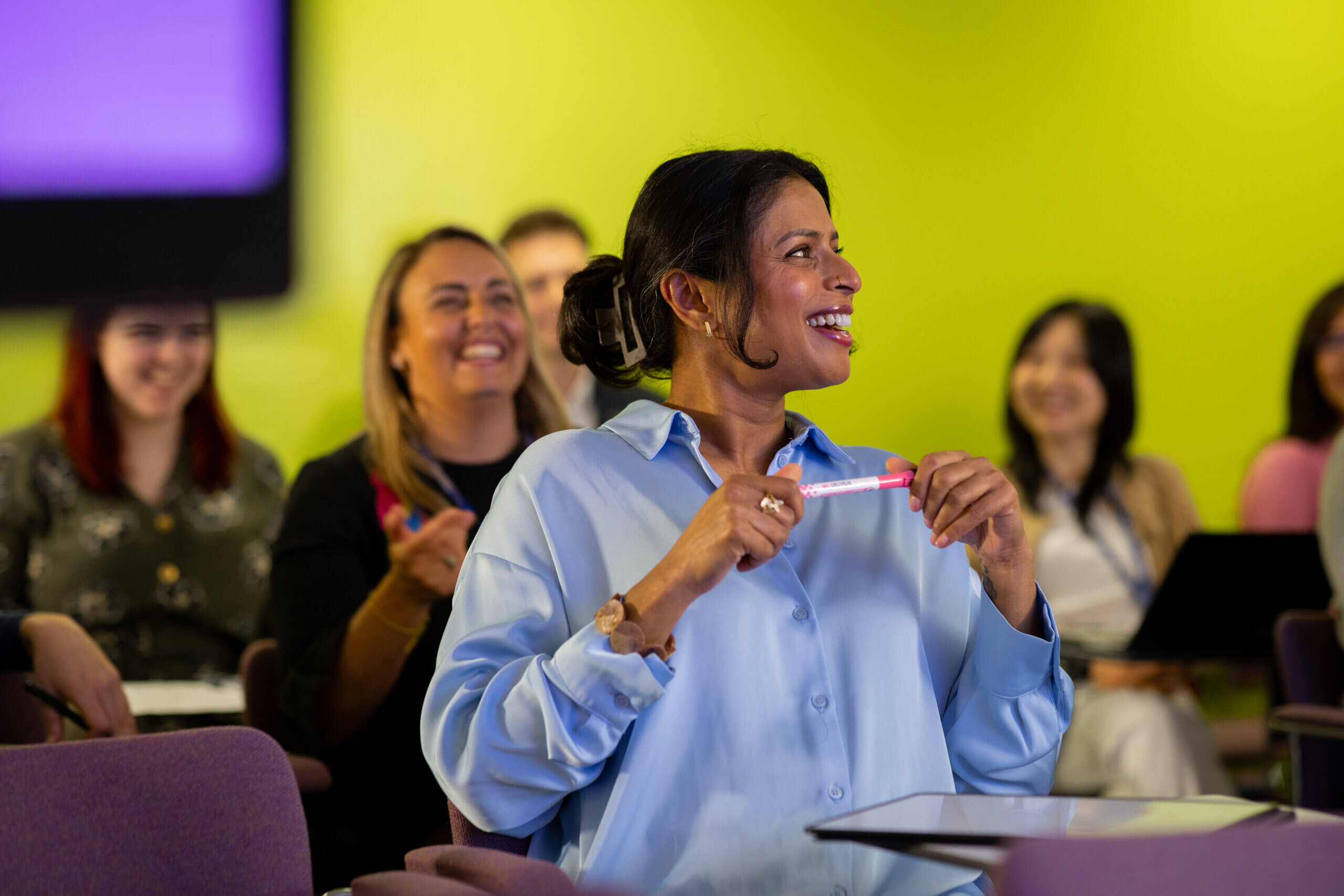 A medium-wide shot of a group of diverse science professionals attending a group seminar in London England, they are leading scientists in their fields of study. Nice camaraderie in a colourful auditorium learning environment, lead female model is laughing off to the right, a real-life scenario. Videos are available similar to this scenario.