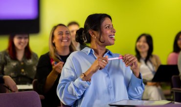 A medium-wide shot of a group of diverse science professionals attending a group seminar in London England, they are leading scientists in their fields of study. Nice camaraderie in a colourful auditorium learning environment, lead female model is laughing off to the right, a real-life scenario. Videos are available similar to this scenario.