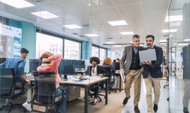 Mature male managers using laptop while walking along computer desks in creative office